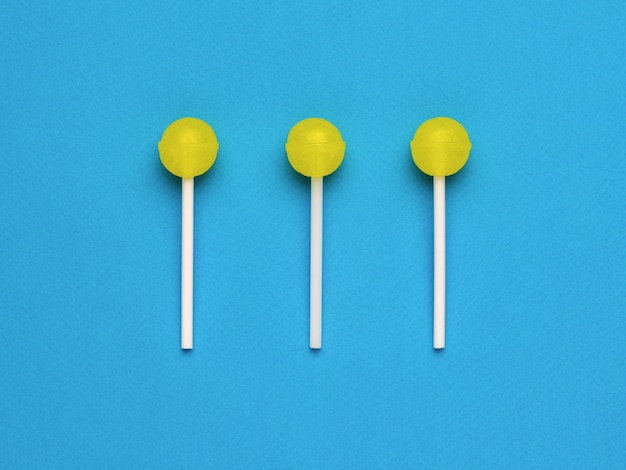 Three bright yellow lollipops on a blue background Minimal concept Sweet candies