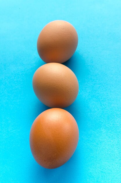 Three brown chicken eggs blue background close up