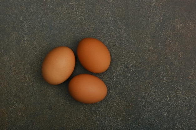 Three brown chicken eggs on dark table