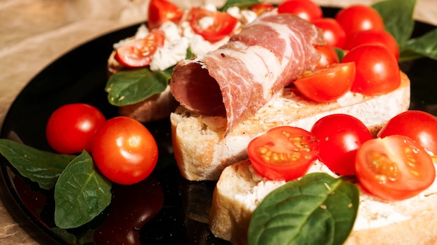 Three bruschetta on a black plate on craft paper. Appetizer with cherry tomatoes, curd cheese, spinach and bacon.