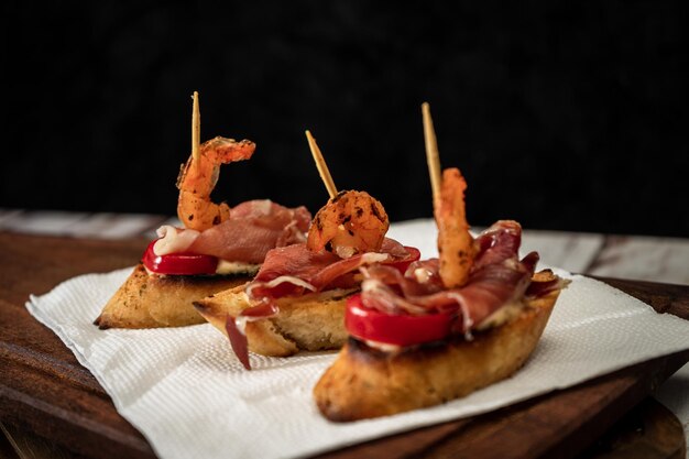 Photo three bruschettas with serrano ham cherry tomato and a grilled shrimp on a wooden board mediterranean food concept