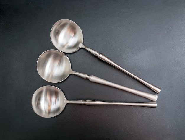 Foto tre cucchiai di zuppa in acciaio inossidabile spazzolati su uno sfondo scuro in primo piano