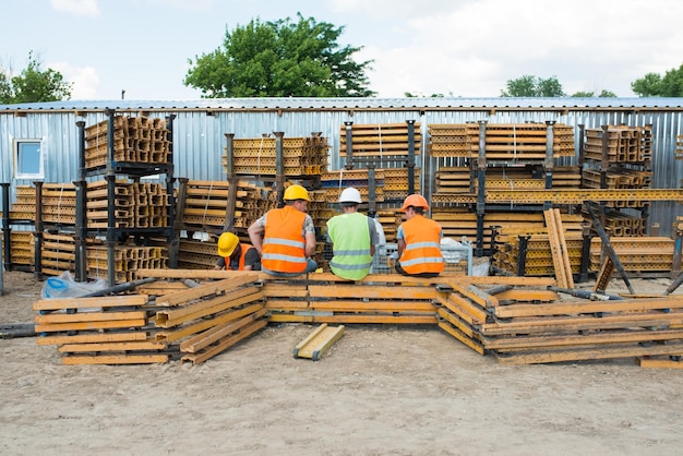 Three builders in helmets at a construction site sit with their backs