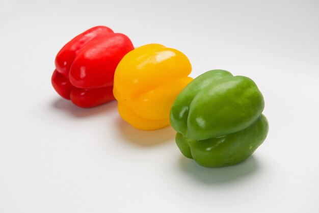 Three bulgarian peppers of different colors lie in a row on a white surface.