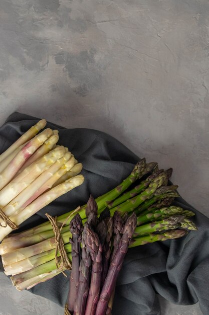 Three bunches of different fresh asparagus isolated on grey. Purple white and green asparagus. Fresh vegetables.