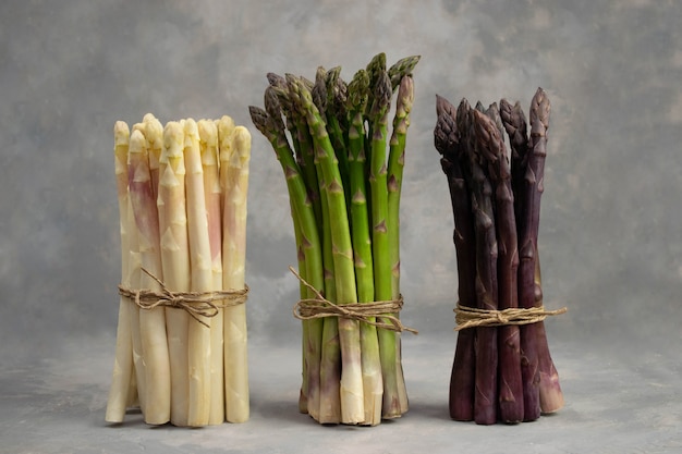 Three bunches of different fresh asparagus isolated on grey. Purple white and green asparagus. Fresh vegetables.