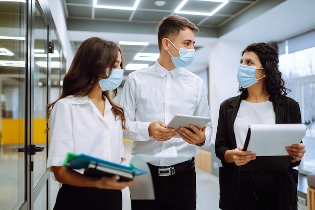 Three business colleagues in protective face mask discussing work related matters on an office