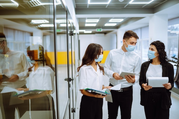 Three business colleagues in protective face mask discussing work related matters on an office