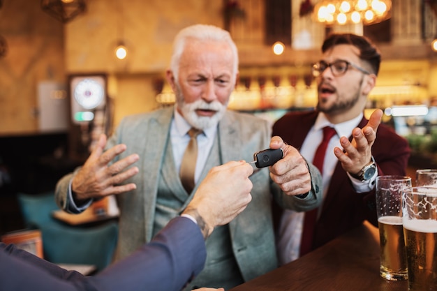 Photo three business people celebrating successfully done job at restaurant. one man taking car key from his drunk business partner.