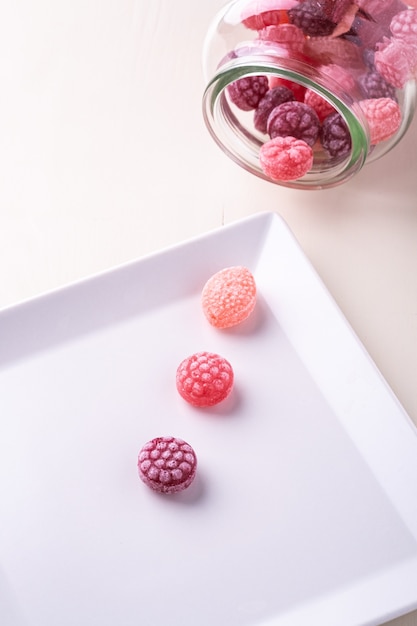 사진 격리 된 흰색 배경에 유리 항아리에 달콤한 딸기의 형태로 사탕 지팡이 과자와 하얀 접시에 3 개의 사탕 지팡이