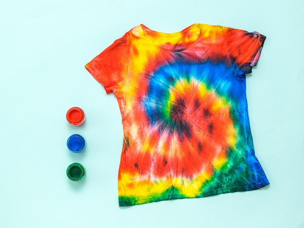 Three cans of paint and a tie dye tshirt on a light blue background Flat lay