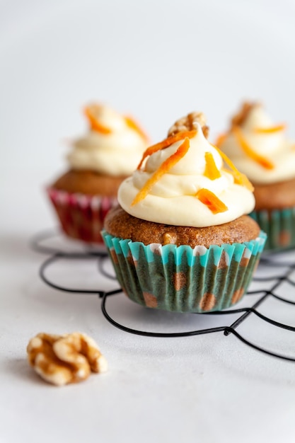 Three carrot cake muffins on a cooling rack on white background with copy space vertical