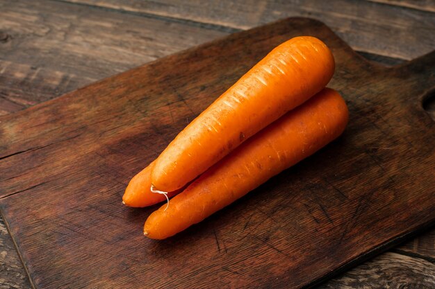 Three carrots on a wooden cutting board. View top. Copy space