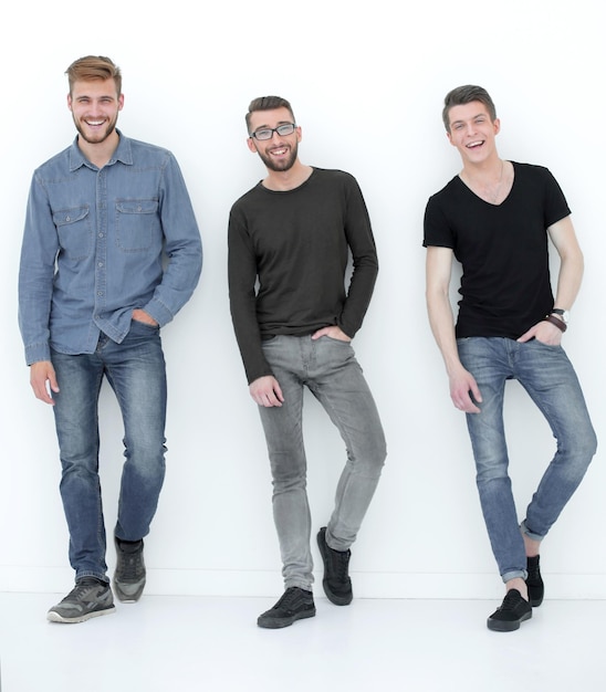 Three casual men having a break and rest standing by the wall in the studio