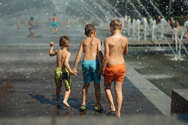 Three caucasian boys going to run throgh splashing fountain on hot summer day in city