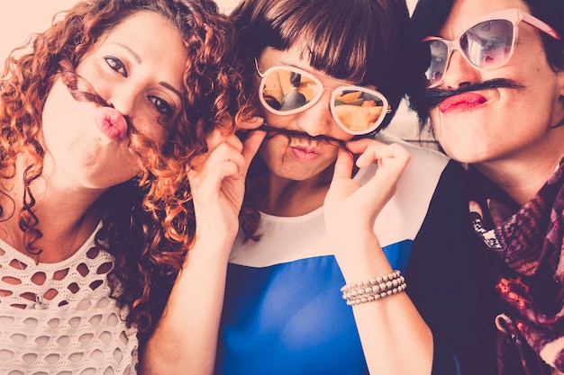 Tre amiche caucasiche stanno insieme in amicizia e follia usando capelli come baffi e concetto di relazione di felicità