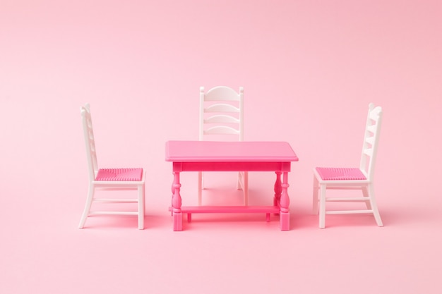 Tre sedie vicino a un tavolo rosso su una superficie rosa