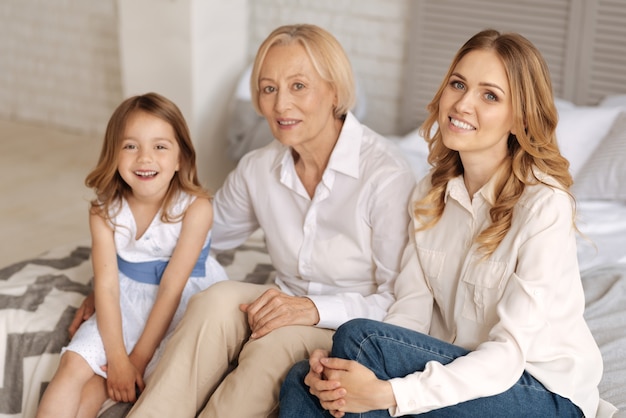 Three charming females of different age spending pleasant time together while bonding to each other on the bed and looking happy to be together