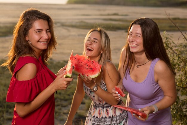 写真 スイカを食べて、ピクニック休暇のコンセプトライフスタイルを笑っている3人の陽気な女の子