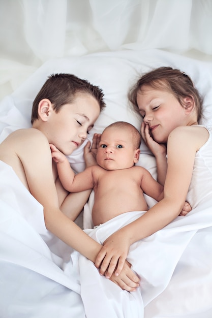 Three cheerful kids at home, newborn baby with brother and sister, happy family, love and friendship concept