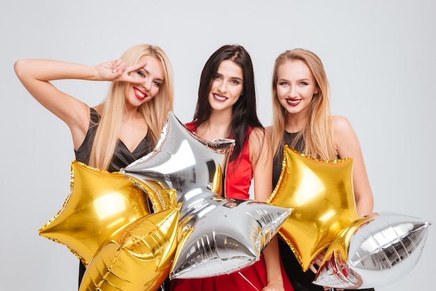 Three cheerful lovely girls holding star shaped balloons over white background