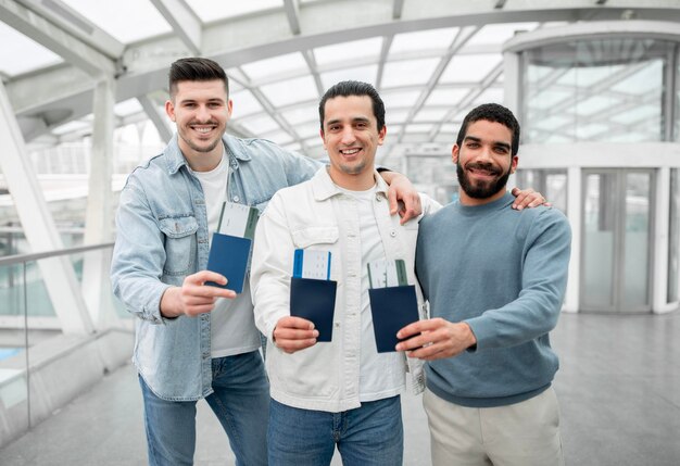 Three cheerful tourists guys showing their boarding passes in airport