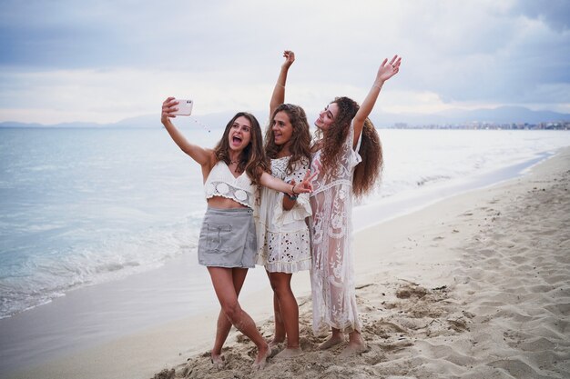 Tre donne allegre che prendono selfie sulla riva della spiaggia