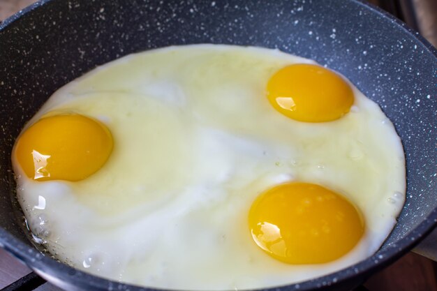 Three chicken eggs are fried in a frying pan