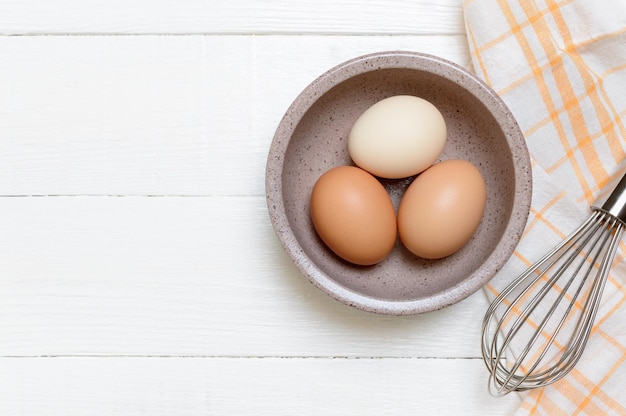 Tre uova di gallina in una ciotola su uno sfondo di legno bianco vista dall'alto ingredienti per la colazione al forno maionese