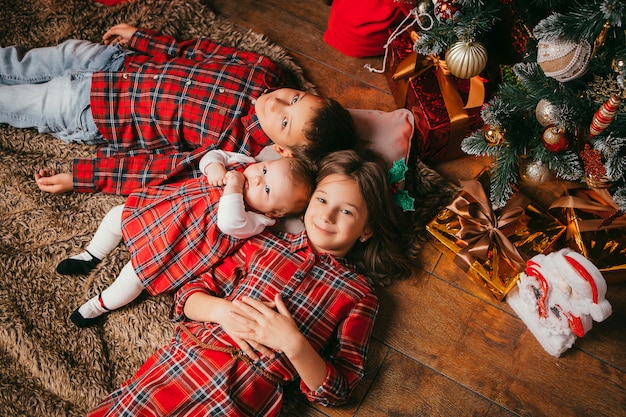 three children lie next to a Christmas tree