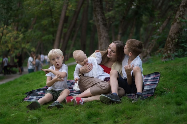 Трое детей и мама наслаждаются пикником летом Концепция единения с детьми Дружелюбные семейные братья и сестры