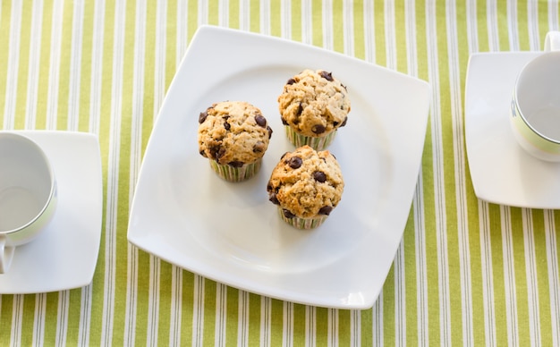 Tre muffin con gocce di cioccolato su un piatto bianco e una tovaglia a strisce verdi a colazione