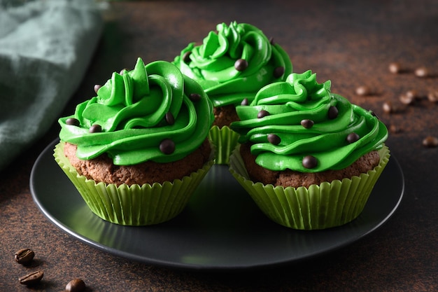 Three chocolate cupcakes with green whipped cream and chocolate sprinkles