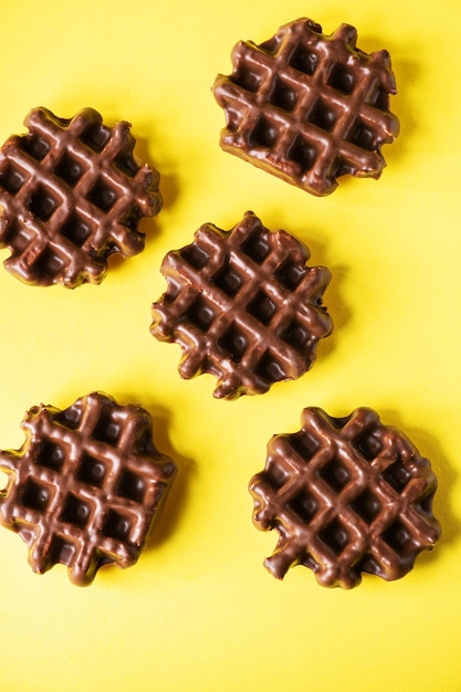 Three chocolate waffles on a yellow background flat lay top view