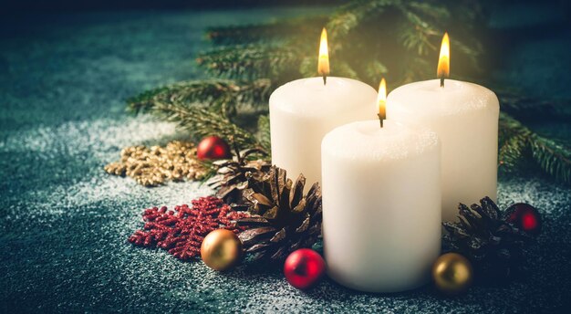 Three Christmas burning candles and decorations on dark turquoise background banner format