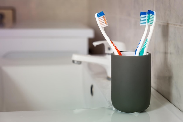 Three colored toothbrushes in a grey glass in a bathroom