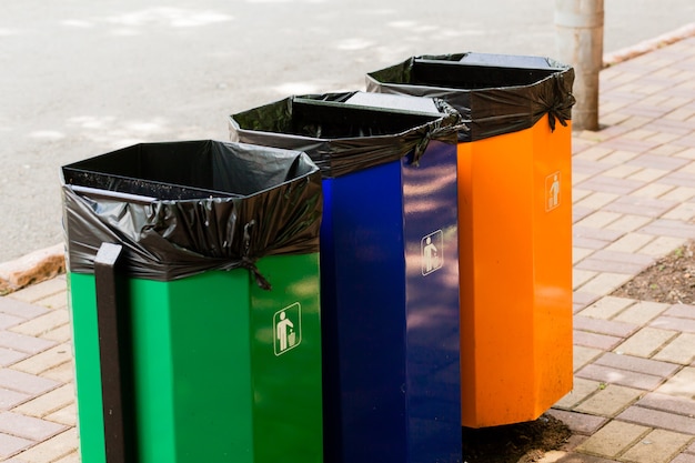 Three colored trash cans in a park next to a footpath.