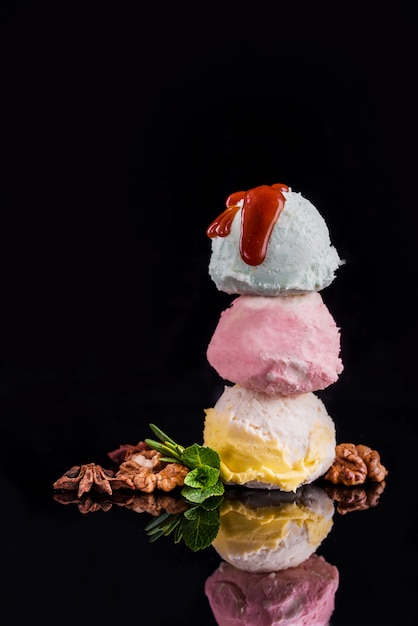 Three colorful balls of delicious ice cream, on a black wall with nuts and a sprig of mint.