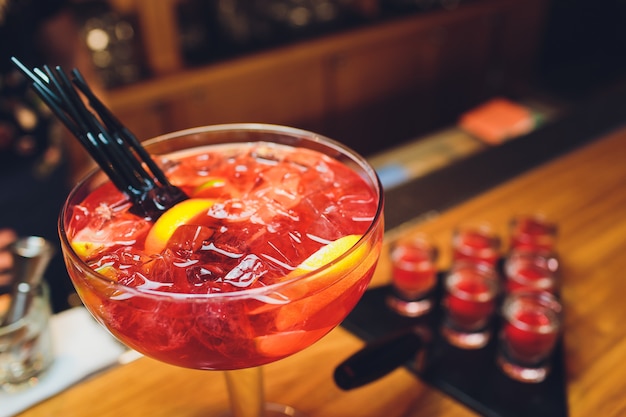 Tre cocktail colorati in grandi bicchieri in un classico ambiente da bar con dozzine di bottiglie di liquore sfocate sullo sfondo.