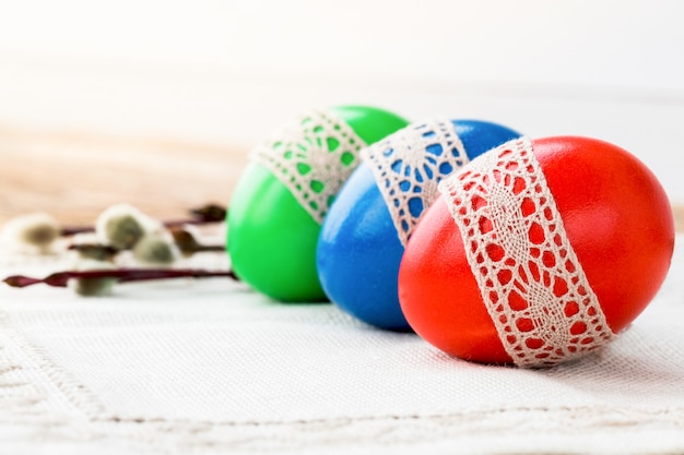 Three colorful Easter eggs on white tablecloth. Copy space, selective focus