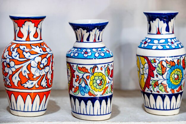 Three colorful vases are on a table, one of which is blue, red, and white.