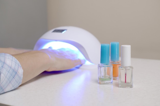 Three colorless transparent nail polish bottles in background of female hands in gel uv led nail white lamp for drying manicure