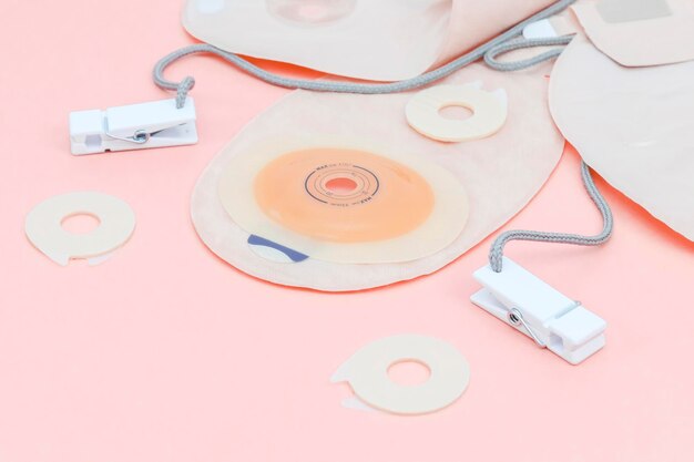 Photo three colostomy bags with medical clips lie on a pale pink background