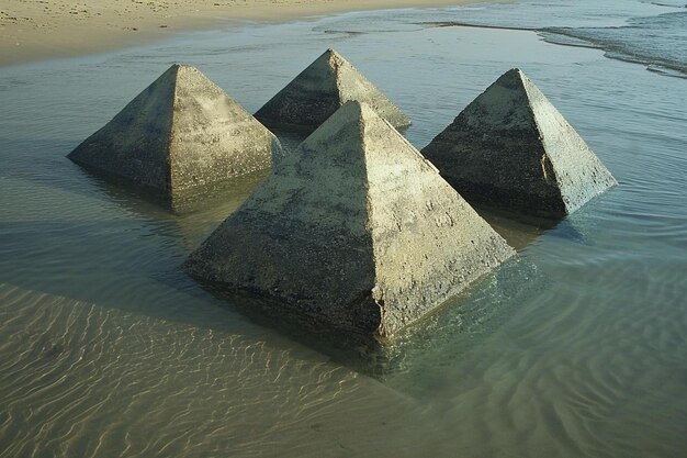 Photo three concrete pyramids in the water on a beach