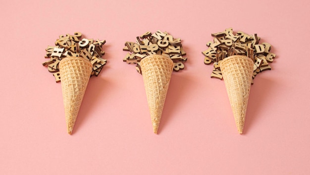 Three cone ice creams formed with a ball of wooden letters on a\
pink background