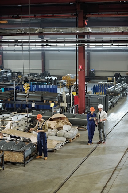 Three contemporary professionals in helmets and workwear carrying out their work in one of factory workshops