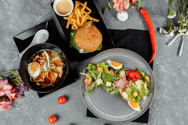 Pranzo di lavoro di tre portate. pranzo con hamburger di spaghetti ramen asiatici e insalata caesar.