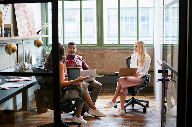 Three coworkers in a team meeting seen through open door