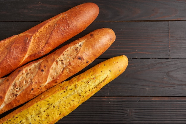 Three crispy french baguettes lie black wooden background