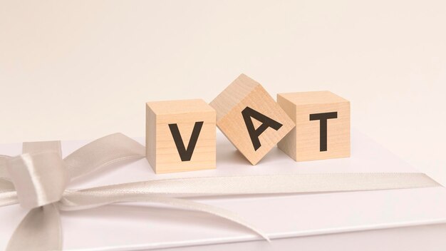 Three cubes with text vat on the white surface of a gift box tied with a light festive ribbon